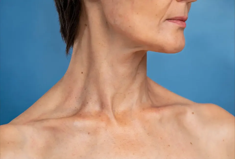 Mature woman gently lifting skin along jawline in front of bathroom mirror